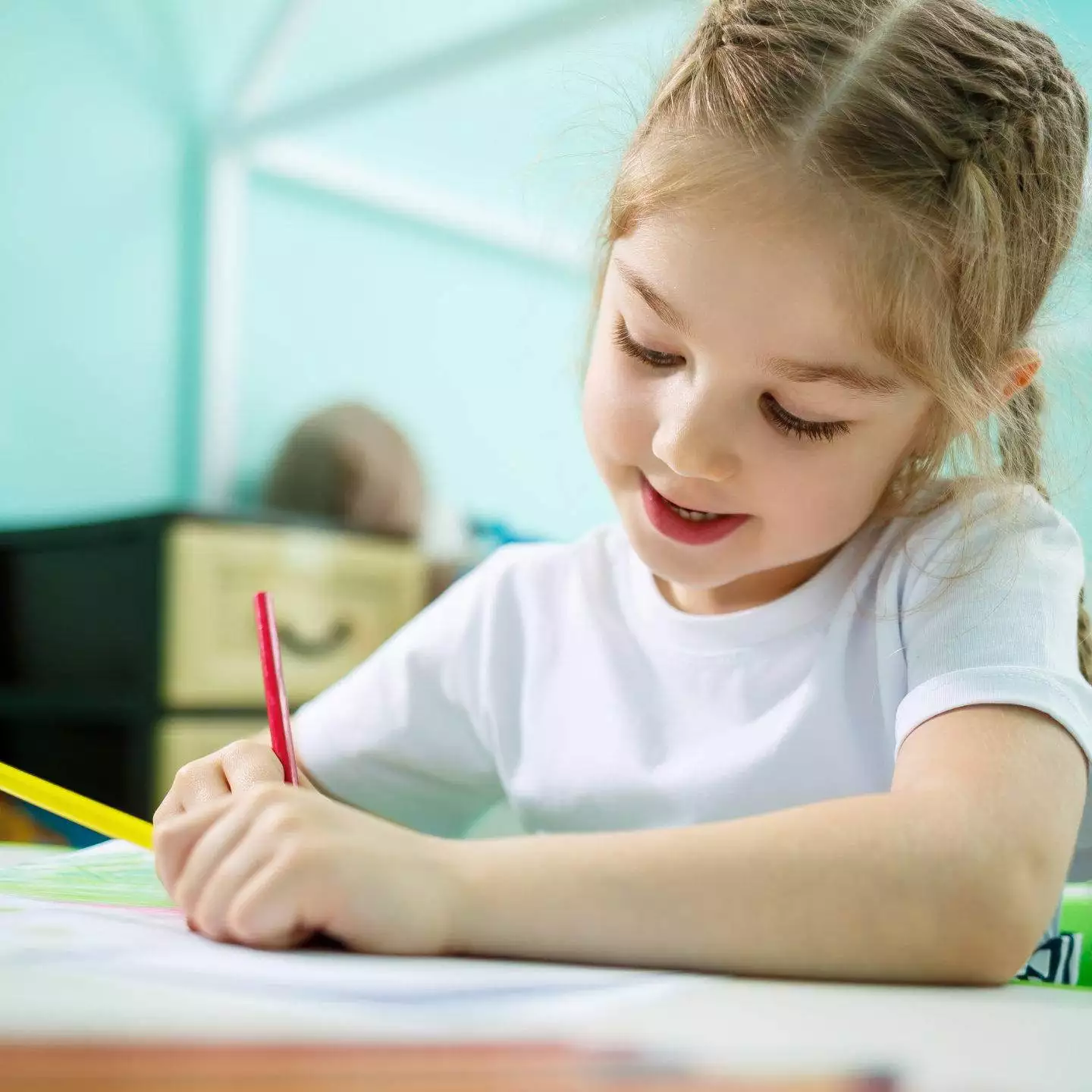 Posebne bilježnice - Namijenjene su djeci s teškoćama u ra… Djevojčica sjedi za stolom i piše u blježnicu